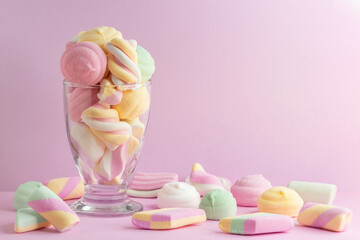 Full glass of candy and sweets and marshmallows with pastel pink background. Lots of soft...