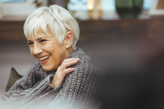 Smiling middle-aged mature gray-haired woman, happy old woman in glasses posing at home indoors, positive unmarried elderly retired woman sitting on sofa in living room portrait headshot