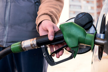 A gray car is refueling at a gas station. The man inserted a fuel pistol into the tank