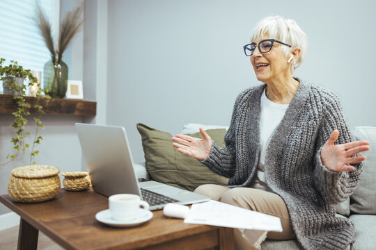 Picture of a smiling mature woman sitting at home talking in a video call with a friend or relative, a happy beautiful older woman talking online using a conference webcam on her computer.