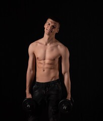 Fototapeta na wymiar young handsome muscular man doing exercises with dumbbells on a black background