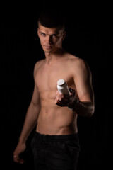 Focus on the details. strong sexy man holds out his hand with a white jar on a black background
