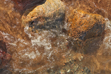 Directly Above Shot of Small Waves Rolling into Beach Dotted with Colorful Rocks and Boulders