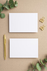 Business concept. Top view vertical photo of two paper sheets gold pen binder clips and eucalyptus on beige background with empty space
