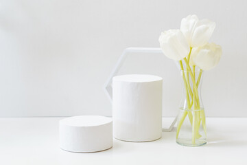 Geometric podium or pedestal with white spring tulips in a vase on a white background. Empty podium...