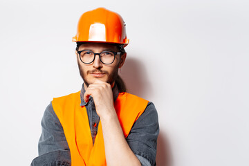 Young thoughtful engineer in orange equipment, wearing glasses on white.