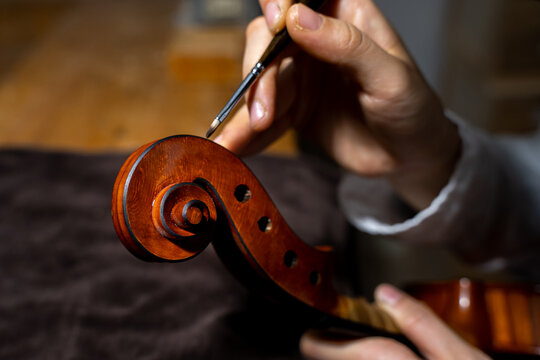 young chinese woman violin maker finishing painting a violin with a thin brush