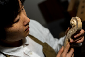 young Chinese female violin maker working with gouge to making a new violin