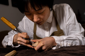 young Chinese female violin maker working with gouge to making a new violin