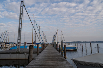 Roped up and covered sailboats on the wooden jetty in the lake in the morning