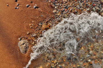 Small Waves Rolling into Sandy Beach Dotted with Colorful Pebbles, Rocks, and Stones