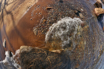 Directly Above Fisheye Shot Small Waves Rolling into Beach Dotted with Colorful Rocks and Boulders