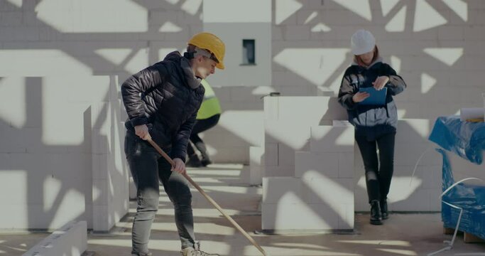 Female construction worker brooming near coworkers
