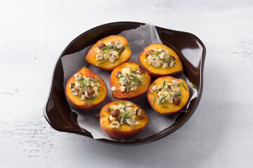 Peaches stuffed with blue cheese with nuts and rosemary in a baking dish on a light gray background. Cooking delicious gourmet dessert