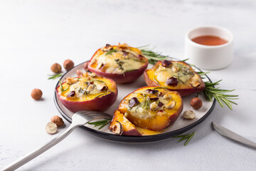 Baked peaches with blue cheese, hazelnuts, rosemary, served with honey on light gray background