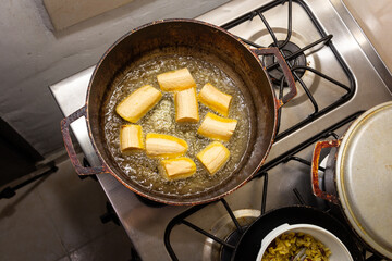 green plantain frying in a pan with oil, view from above