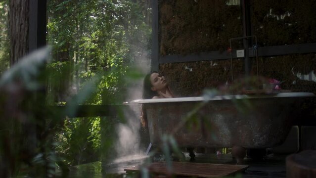 A girl in a bathtub in a forest during the rain. Beautiful young woman relaxing in the bathroom in the tropical rainforest jungle in a luxury spa while raining