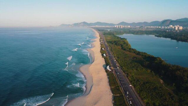 Aerial view of Reserva beach, Marapendi lagoon and car traffic on Lucio Costa avenue. Barra da Tijuca and Recreio, in Rio de Janeiro, Brazil. Sunrise. Sunny day. Drone take. Praia da Reserva.
