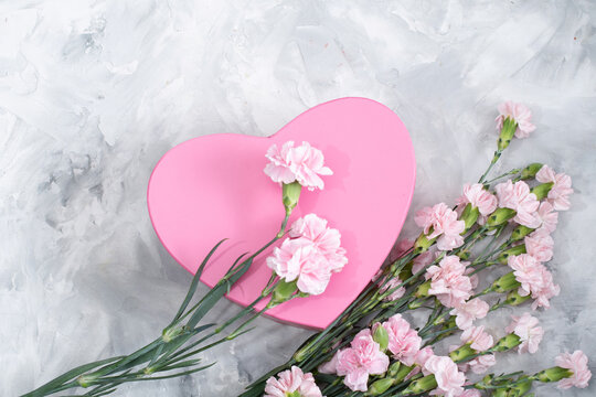 pink carnations and a heart-shaped box on a light gray cement background, a gift