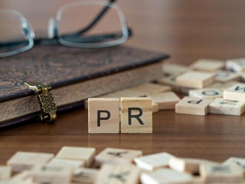 the acronym pr for progress report word or concept represented by wooden letter tiles on a wooden table with glasses and a book