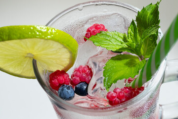 Refreshing summer cocktail with ice, lime and berries in a glass with a straw