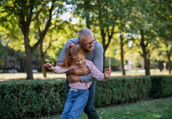 Happy grandfather hugging his little granddaughter outdoors in park.