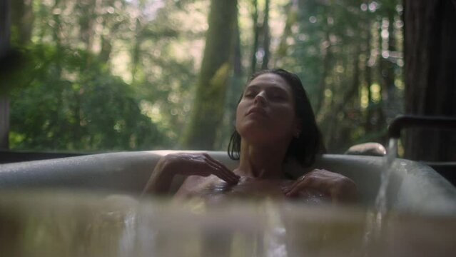 A girl in a bathtub in a forest during the rain. Beautiful young woman relaxing in the bathroom in the tropical rainforest jungle in a luxury spa while raining