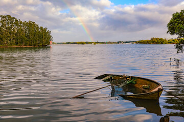 Tranquil water scene with partially sunk row boat in Wallis Lake at Forster NSW with rainbow in...
