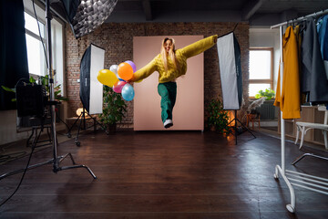 Fashion studio portrait of a happy young woman with balloons jumping, backstage of photoshooting .