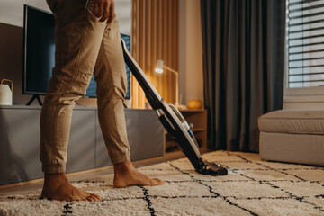 Lowsection of man hoovering carpet with vacuum cleaner in living room - obrazy, fototapety, plakaty
