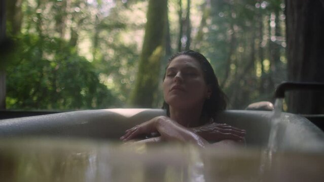 A girl in a bathtub in a forest during the rain. Beautiful young woman relaxing in the bathroom in the tropical rainforest jungle in a luxury spa while raining