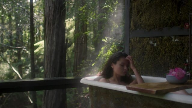 A girl in a bathtub in a forest during the rain. Beautiful young woman relaxing in the bathroom in the tropical rainforest jungle in a luxury spa while raining