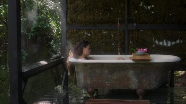 A girl in a bathtub in a forest during the rain. Beautiful young woman relaxing in the bathroom in the tropical rainforest jungle in a luxury spa while raining