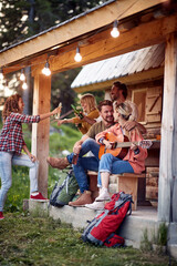 A group of cheerful friends having fun at cottage porch in the forest. Vacation, nature, cottage,...