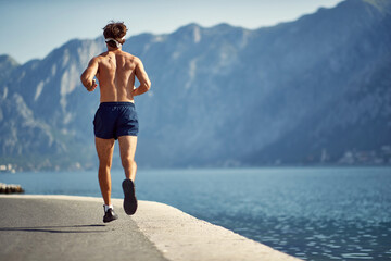 Young man running on jetty by water. Outdoors workout. Sport, vitality, recreation concept.