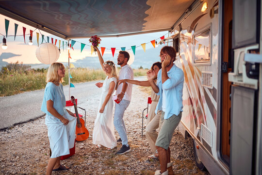 Newlyweds and friends dancing in front of decorated camper rv. Celebration of newlywed love couple. Wedding ceremony, love, nature concept