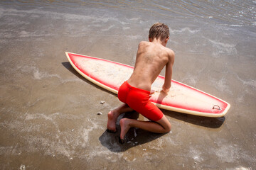 Young male surfer waxing his surfboard on the beach