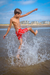 Young boy on the beach kicking and splashing in the water