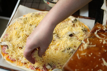 Defocus ingredients for pizza on dough. Female hand cooking. Red tomato sauce, sausages, sweet corn, mushrooms, cheese. Homemade pizza. Base of Margarita. Home culinary, fast food.  Out of focus