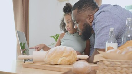 African America father and daughter learning recipe cooking online on laptop computer for cooking bakery or bread at home, dad and child preparing food, domestic life, family and lifestyles concept.