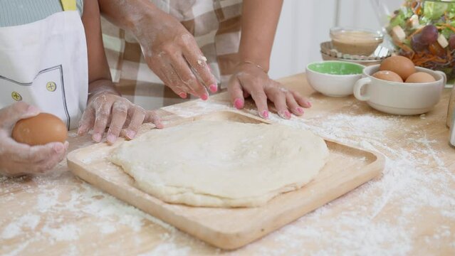 Closeup hands of African American family with daughter add egg to flour and thresh for cooking with father and mother together in the kitchen at home, parent and little child preparing food with fun.