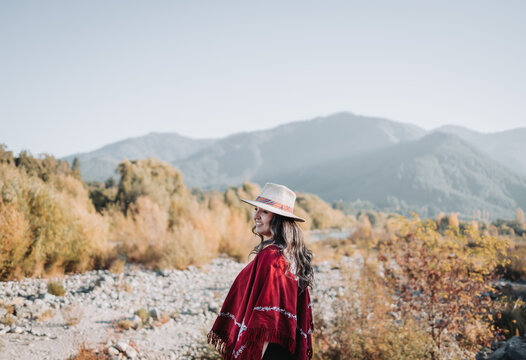 Traditional latin american woman wearing a red poncho and a hat seen from behind, in a natural space. Womens empowerment