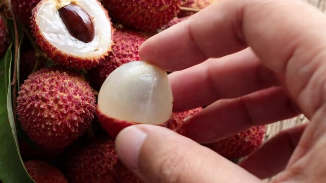 Fresh ripe lychee fruit and peeled lychee with green leaves on wooden background. 