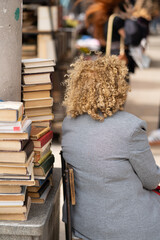 Back view of senior woman selling old books on the city street. Female bookseller in Tbilisi