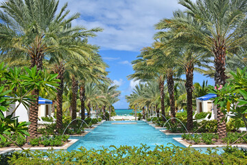 Tropical resort style pool lined with palm trees and cabanas