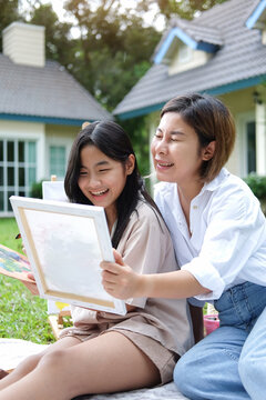 Happy young mother and her daughter painting picture, having fun together and spending their leisure time outdoors.