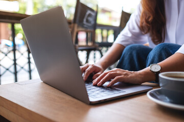 Closeup image of a woman working and typing on laptop computer keyboard with coffee cup on the table