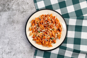 Red chicken pasta with herbs, tomatoes and cheese on a white round plate on a dark gray background. Top view, flat lay