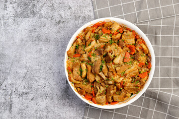Oven baked pork belly with rice and vegetables in a white baking dish on a dark grey background. Top view, flat lay