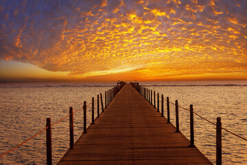 Obraz premium orange sky with spindrift clouds on sunrise in Egypt and wooden bridge in sea